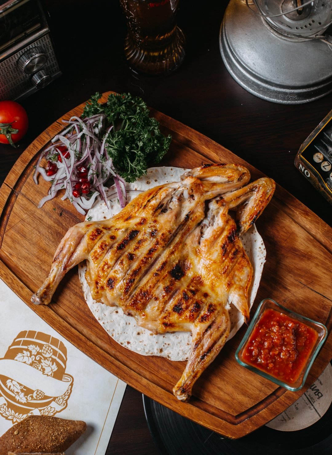 top view of traditional caucasian cuisine of grilled chicken tabaka with red onion herbs and tomato sauce adjika